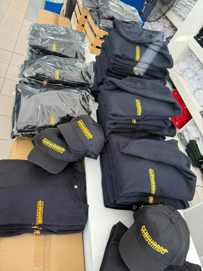 Pantalones y gorras azul oscuro con bordado dorado, apilados sobre una mesa